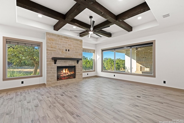 unfurnished living room with beamed ceiling, light hardwood / wood-style flooring, a stone fireplace, and coffered ceiling