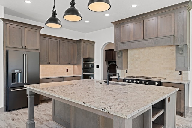 kitchen featuring a center island with sink, sink, appliances with stainless steel finishes, decorative light fixtures, and light hardwood / wood-style floors