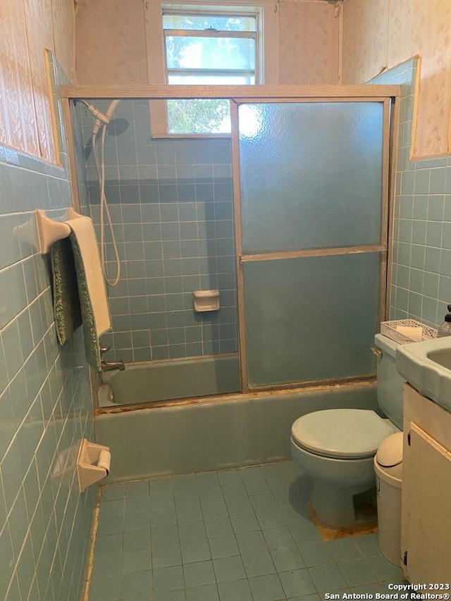 full bathroom featuring combined bath / shower with glass door, vanity, toilet, and tile walls