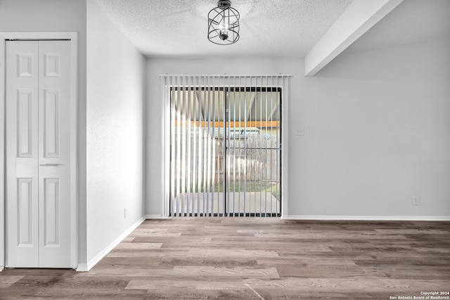 unfurnished room featuring beam ceiling, light hardwood / wood-style floors, and a textured ceiling