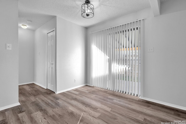 empty room with wood-type flooring, a textured ceiling, and a notable chandelier