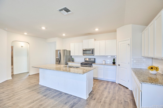 kitchen featuring white cabinets, a center island with sink, light stone countertops, appliances with stainless steel finishes, and light hardwood / wood-style floors