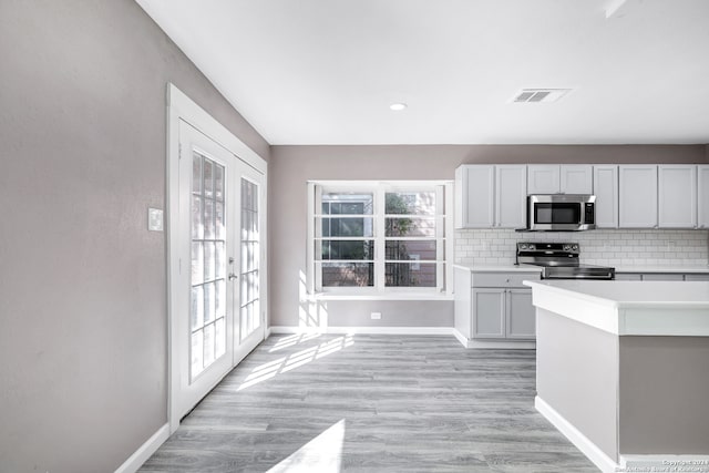 kitchen with french doors, white cabinets, decorative backsplash, light wood-type flooring, and stainless steel appliances