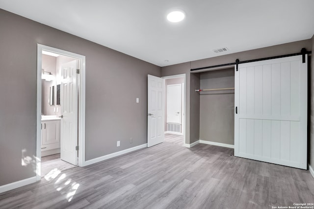 unfurnished bedroom with a barn door, ensuite bathroom, light hardwood / wood-style flooring, and a closet