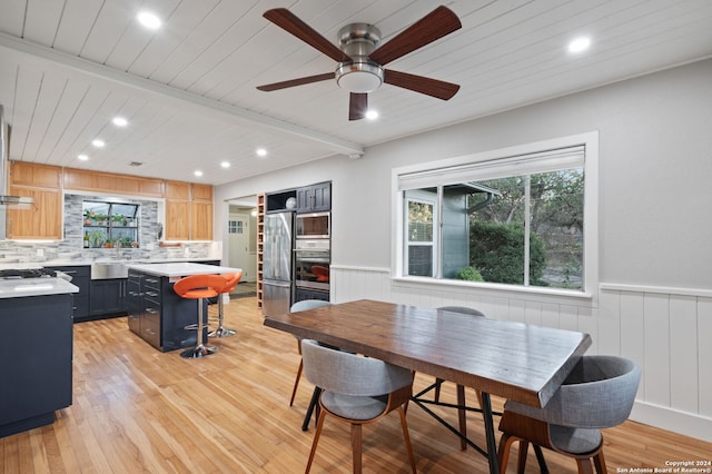 dining space featuring ceiling fan, light hardwood / wood-style floors, sink, and beam ceiling