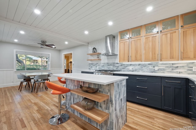 kitchen featuring ceiling fan, a center island, wall chimney exhaust hood, and wooden ceiling