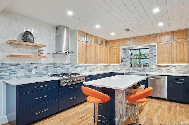 kitchen with a kitchen bar, stainless steel appliances, wall chimney range hood, a center island, and light hardwood / wood-style floors