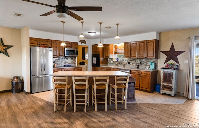 kitchen with appliances with stainless steel finishes, light hardwood / wood-style flooring, a kitchen island, and hanging light fixtures