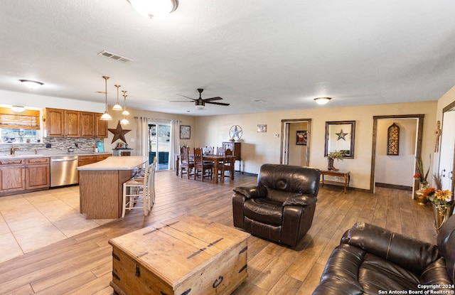 living room with ceiling fan, sink, light hardwood / wood-style floors, and a textured ceiling