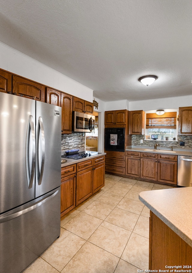 kitchen featuring tasteful backsplash, a textured ceiling, sink, black appliances, and light tile patterned flooring