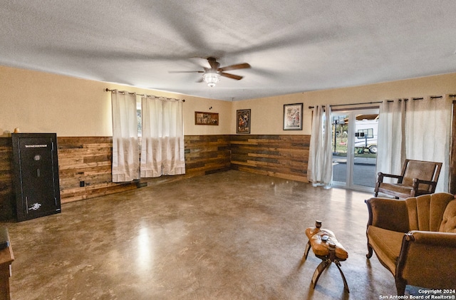 living area with ceiling fan, a textured ceiling, wooden walls, and concrete floors