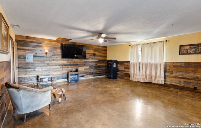 living area featuring wooden walls, ceiling fan, and a textured ceiling