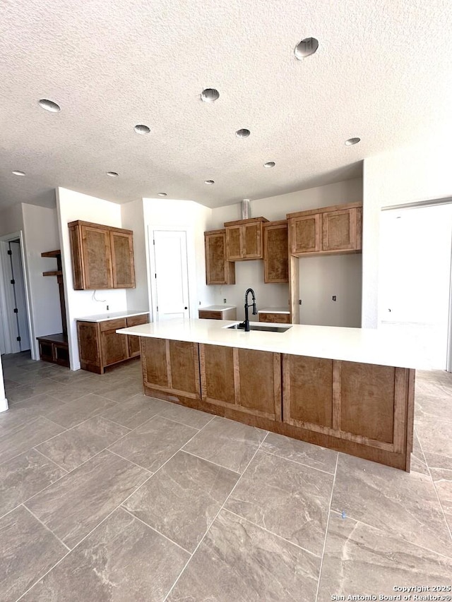 177 Pine Valley Dr, La Vernia, TX 78121 - kitchen featuring a sink, a textured ceiling, brown cabinets, a large island with sink, and light countertops