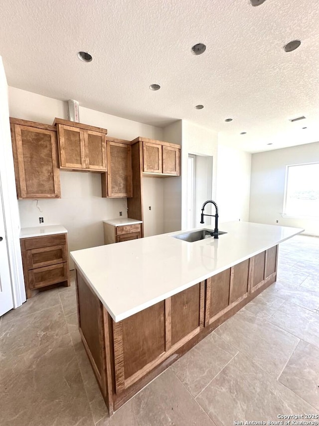 177 Pine Valley Dr, La Vernia, TX 78121 - kitchen with a sink, a large island with sink, a textured ceiling, brown cabinetry, and light countertops