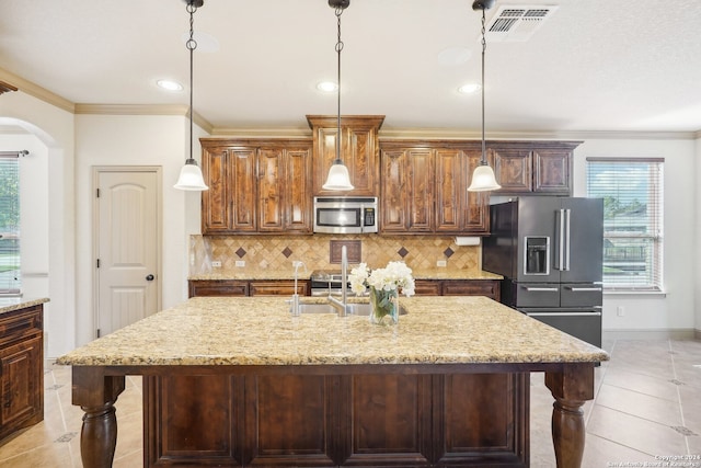 kitchen with pendant lighting, decorative backsplash, a center island with sink, appliances with stainless steel finishes, and ornamental molding