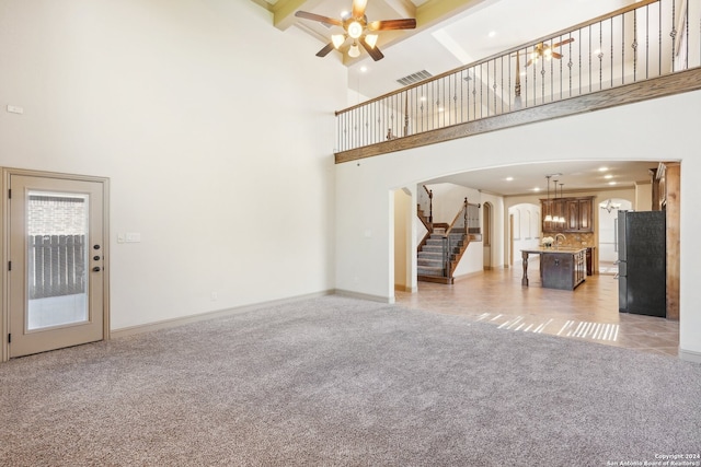 unfurnished living room with beamed ceiling, a high ceiling, ceiling fan, and sink