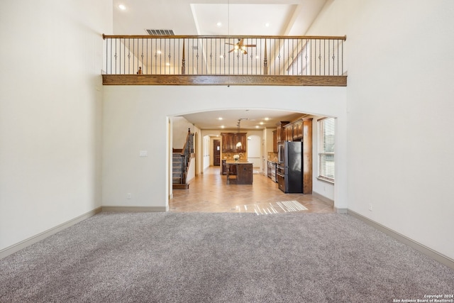 unfurnished living room featuring light carpet and a high ceiling