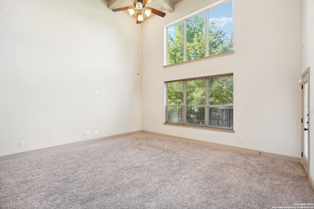 carpeted spare room featuring beamed ceiling, ceiling fan, and a high ceiling