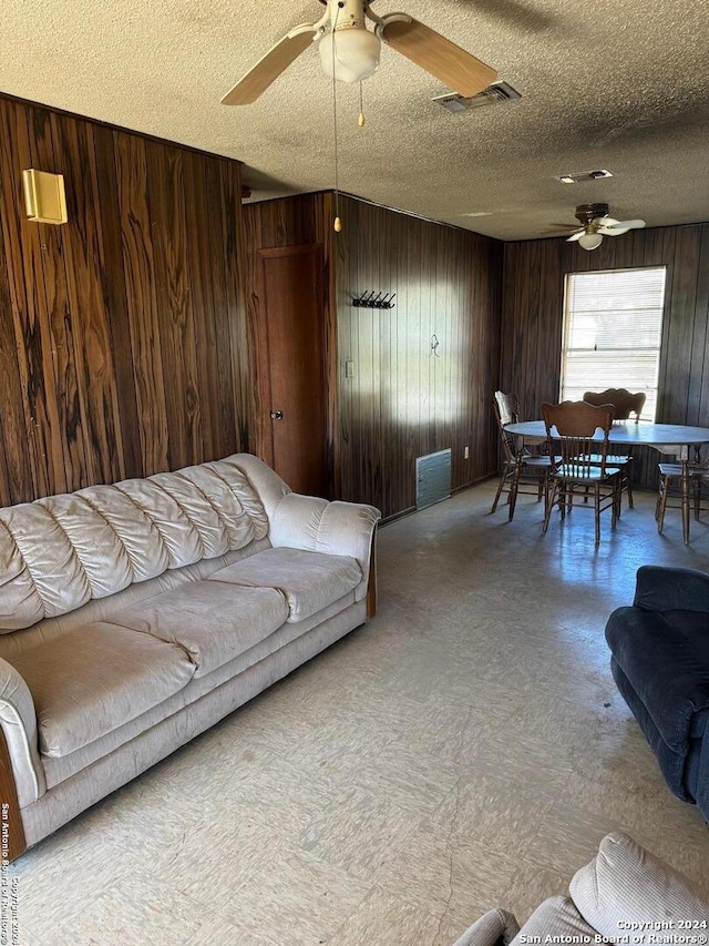 living room featuring wooden walls, ceiling fan, and a textured ceiling