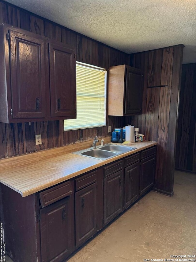 kitchen featuring a textured ceiling, dark brown cabinets, and sink