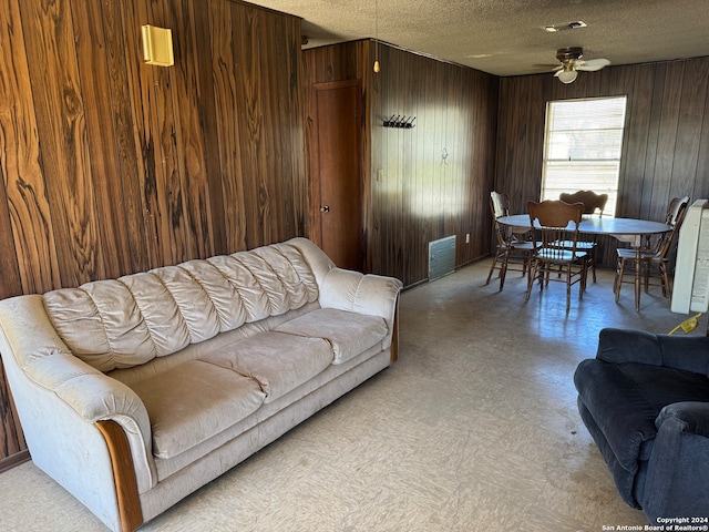 living room featuring ceiling fan, wood walls, and a textured ceiling