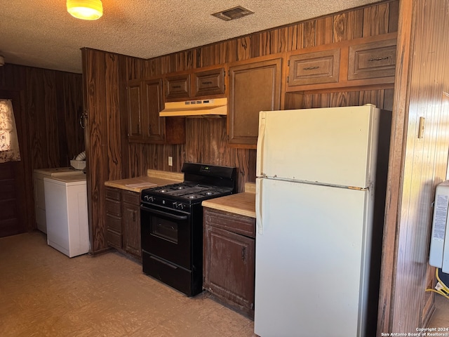 kitchen with gas stove, washer / clothes dryer, wood walls, white fridge, and a textured ceiling