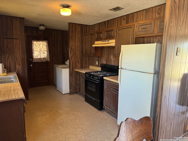 kitchen featuring gas stove, white refrigerator, washer / clothes dryer, a textured ceiling, and wooden walls