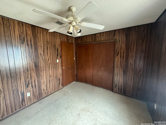 empty room featuring ceiling fan, a textured ceiling, and wooden walls