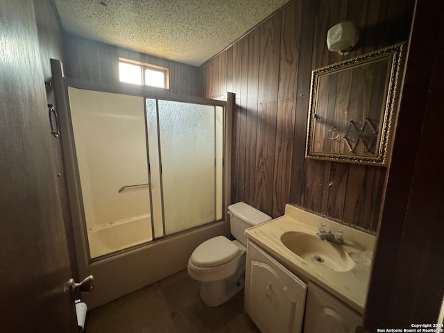 full bathroom with vanity, shower / bath combination with glass door, wooden walls, toilet, and a textured ceiling