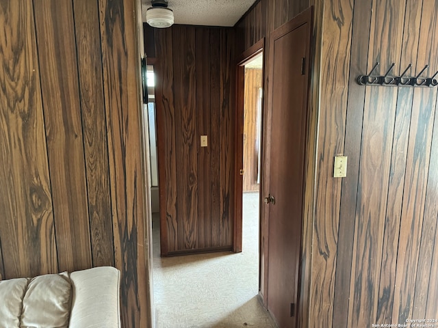 corridor with carpet flooring, a textured ceiling, and wooden walls