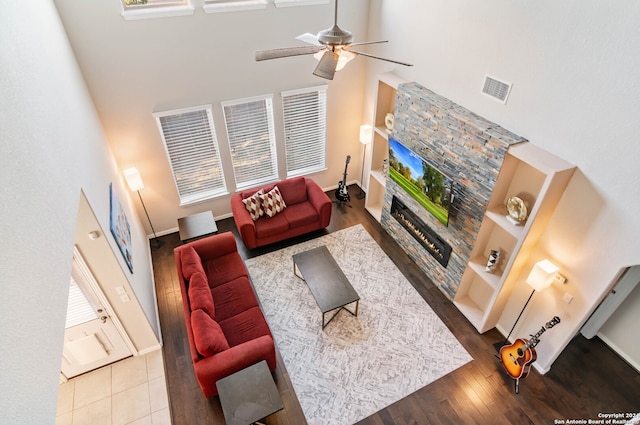 living room featuring ceiling fan, a fireplace, a towering ceiling, and hardwood / wood-style flooring