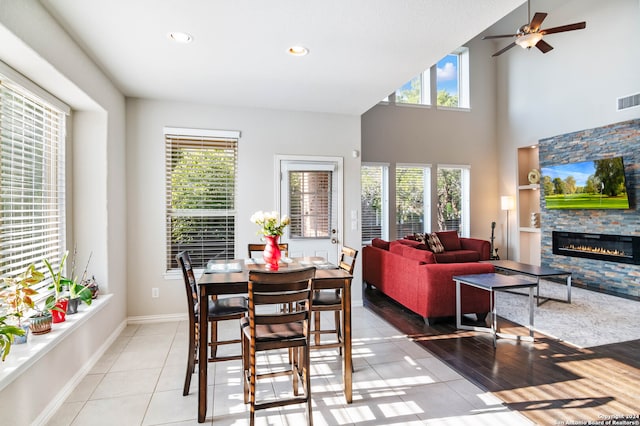 dining area featuring a fireplace, a high ceiling, light hardwood / wood-style flooring, and ceiling fan