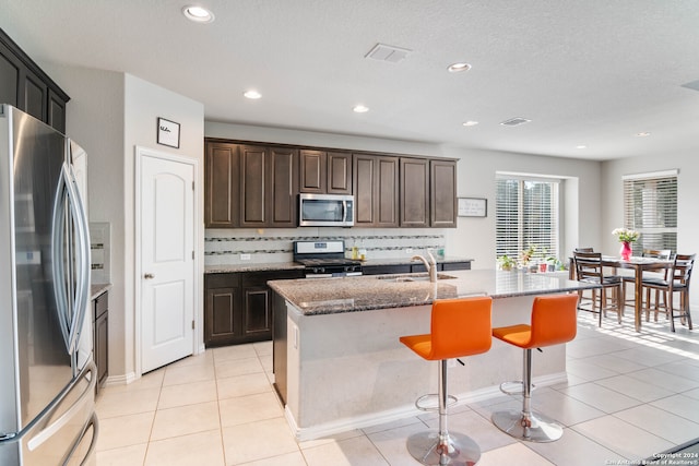 kitchen featuring appliances with stainless steel finishes, tasteful backsplash, sink, light tile patterned floors, and an island with sink