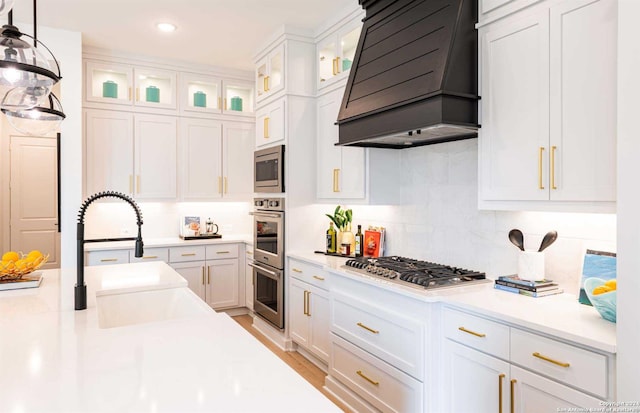 kitchen featuring decorative light fixtures, white cabinetry, custom range hood, and stainless steel appliances