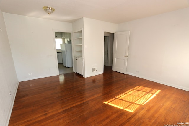 empty room with built in shelves and dark wood-type flooring