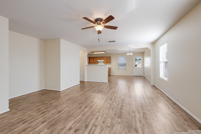 unfurnished living room with ceiling fan with notable chandelier and light wood-type flooring