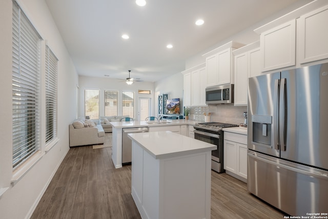 kitchen featuring hardwood / wood-style floors, a center island, decorative backsplash, kitchen peninsula, and stainless steel appliances