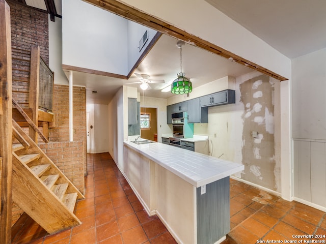 kitchen with kitchen peninsula, a kitchen breakfast bar, black electric stovetop, ceiling fan, and tile counters