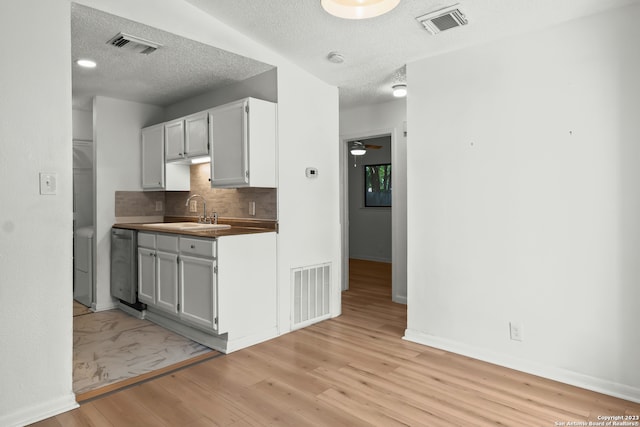 kitchen with ceiling fan, sink, backsplash, a textured ceiling, and light wood-type flooring