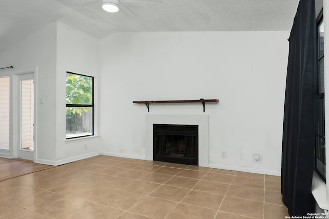 unfurnished living room with ceiling fan, a tiled fireplace, light tile patterned floors, and vaulted ceiling