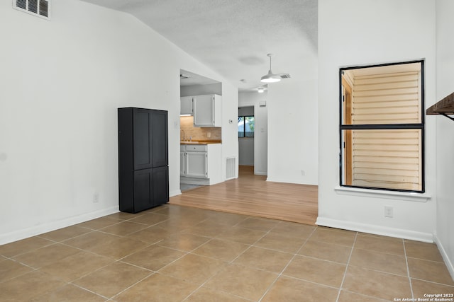 unfurnished living room with a textured ceiling, lofted ceiling, and light tile patterned flooring