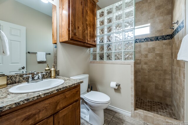 bathroom with tile patterned flooring, vanity, toilet, and tiled shower