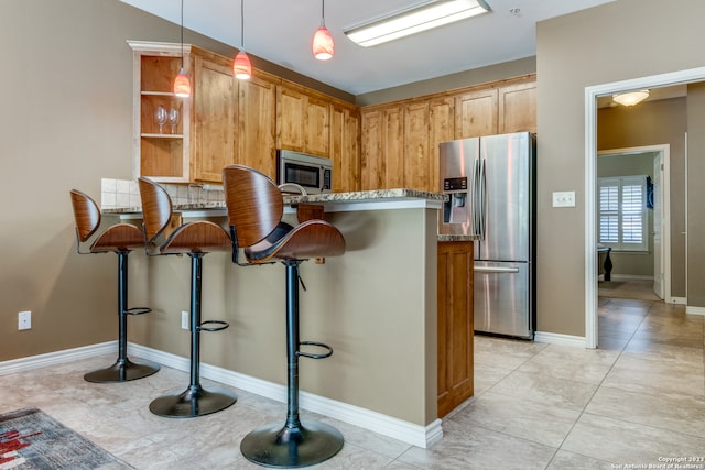 kitchen featuring light stone counters, kitchen peninsula, decorative light fixtures, a breakfast bar area, and appliances with stainless steel finishes