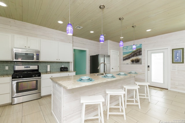 kitchen with a center island with sink, wood walls, and appliances with stainless steel finishes