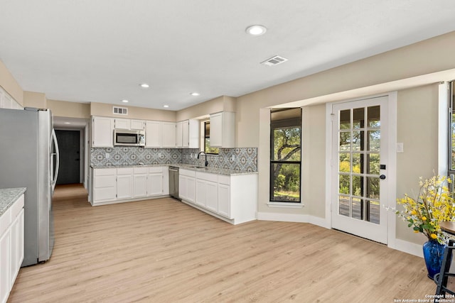 kitchen with tasteful backsplash, white cabinetry, light hardwood / wood-style floors, and appliances with stainless steel finishes