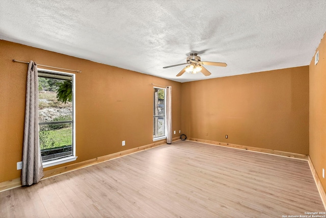 empty room with ceiling fan, light wood-type flooring, and a textured ceiling