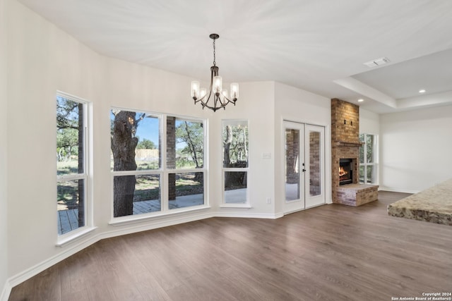 unfurnished living room with french doors, hardwood / wood-style flooring, a brick fireplace, and a notable chandelier