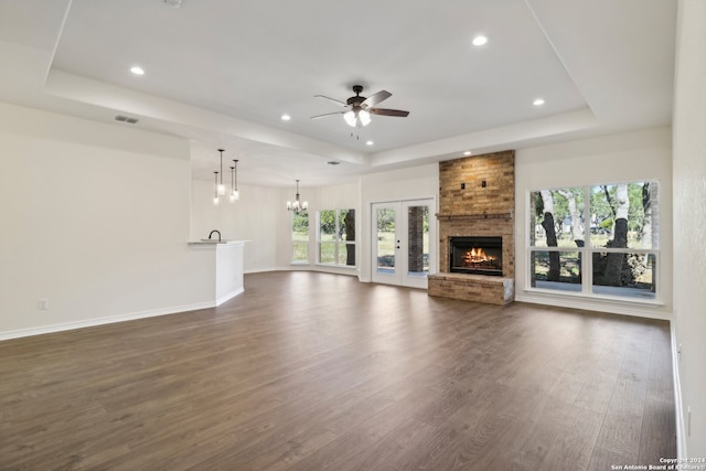 unfurnished living room featuring dark hardwood / wood-style floors, a fireplace, ceiling fan with notable chandelier, and a tray ceiling