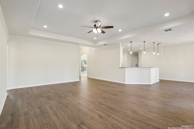 unfurnished living room featuring a raised ceiling, ceiling fan, and dark hardwood / wood-style flooring