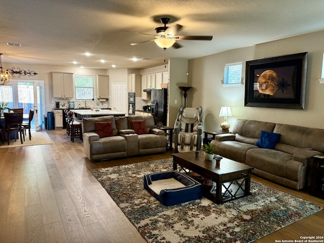 living room featuring a textured ceiling, light hardwood / wood-style floors, and ceiling fan with notable chandelier